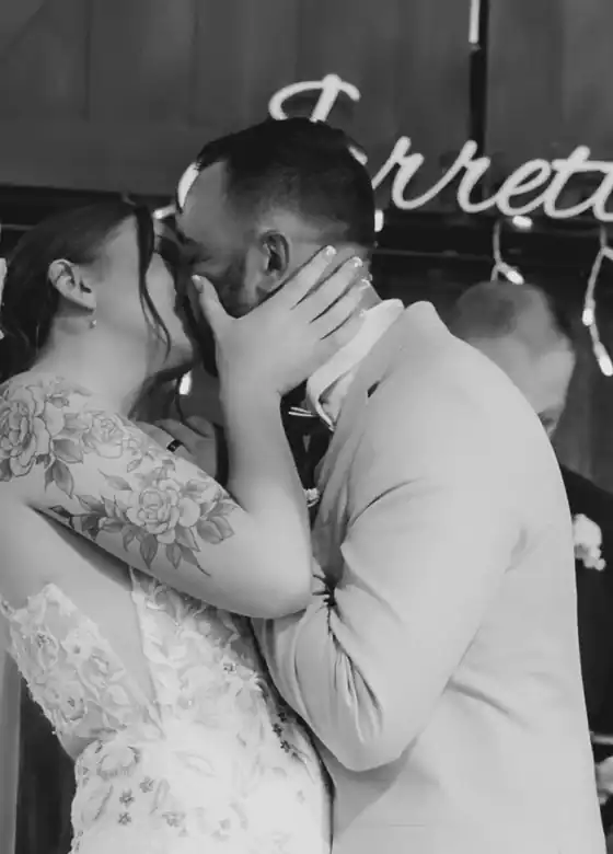 A bride and groom kissing under neon lettering at their reception